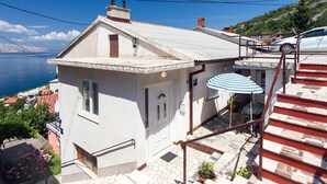 A white house with a tiled roof, a small porch with a striped umbrella, and a view of the sea.