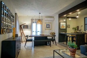 A modern kitchen with a central island, a dining area with a dark-colored table and chairs, and a living area with a glass coffee table and a potted plant. - Charming Home Near San Miguel Main Plaza (San Miguel de Allende)