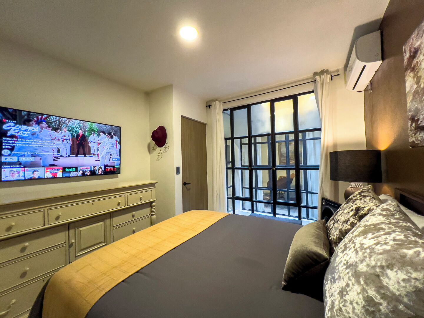 A hotel room with a large bed, a TV mounted on the wall, a window with a view, and a door.