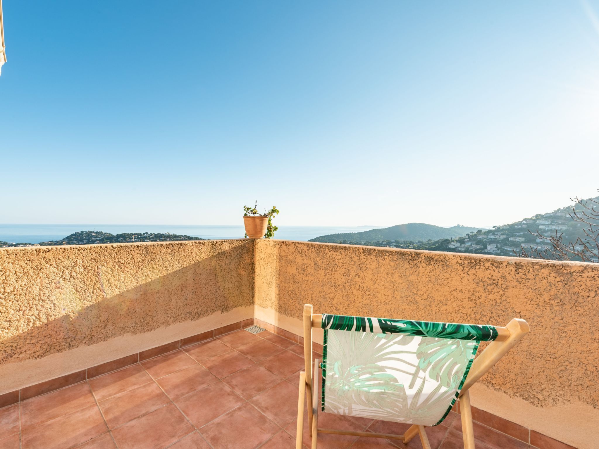 Un balcon avec des carreaux de terre cuite, une chaise en bois et une plante en pot.