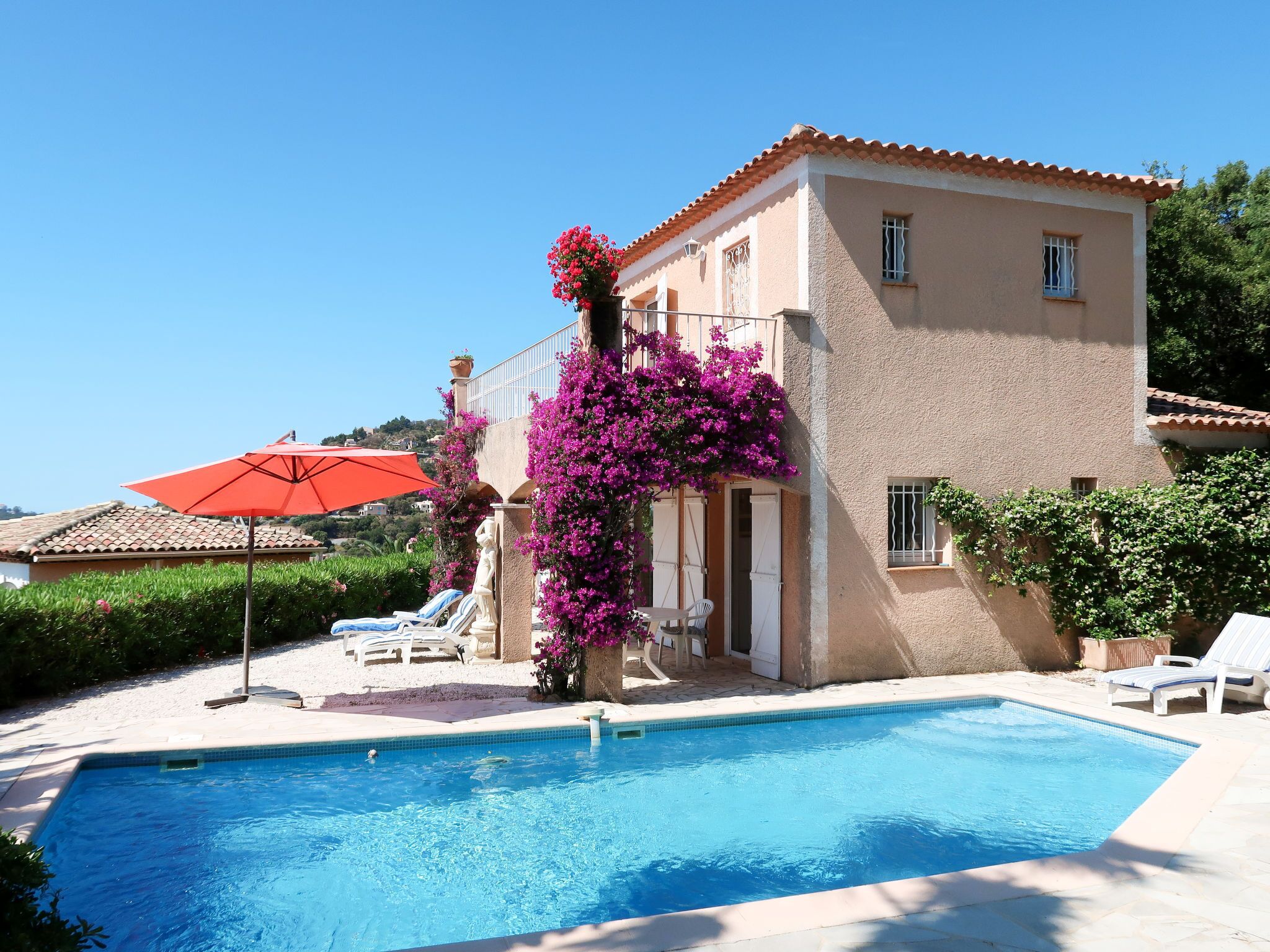 A pool area with a clear blue pool, lounge chairs, and a red umbrella.