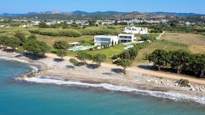 A coastal property with modern architecture, a beach, and a view of the surrounding landscape. - Stunning beachfront retreat, private tennis court & infinity pool (Rhodes)