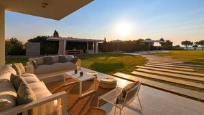 A modern outdoor living area with a sofa set, a table, and chairs, a pergola, and a view of the sea. - Stunning beachfront retreat, private tennis court & infinity pool (Rhodes)