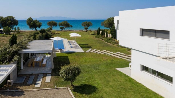 A modern building with a pool area, outdoor seating, and a view of the sea. - Stunning beachfront retreat, private tennis court & infinity pool (Rhodes)