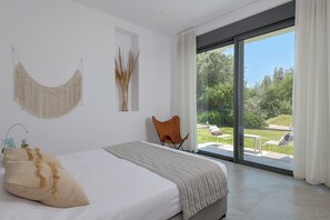 A modern bedroom with a large bed, a view of the outdoors, and a minimalist decor.