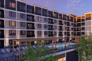 A modern hotel with multiple floors, a rooftop pool area with lounge chairs, and a covered seating area.