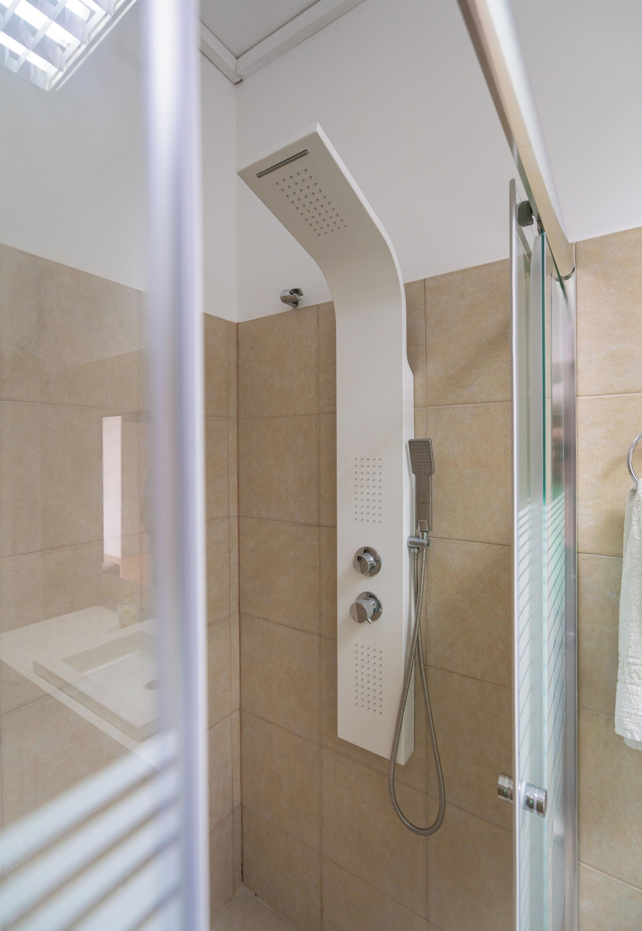 Un espace douche moderne doté d’une porte en verre, de carreaux de couleur beige et d’un pommeau de douche à main.
