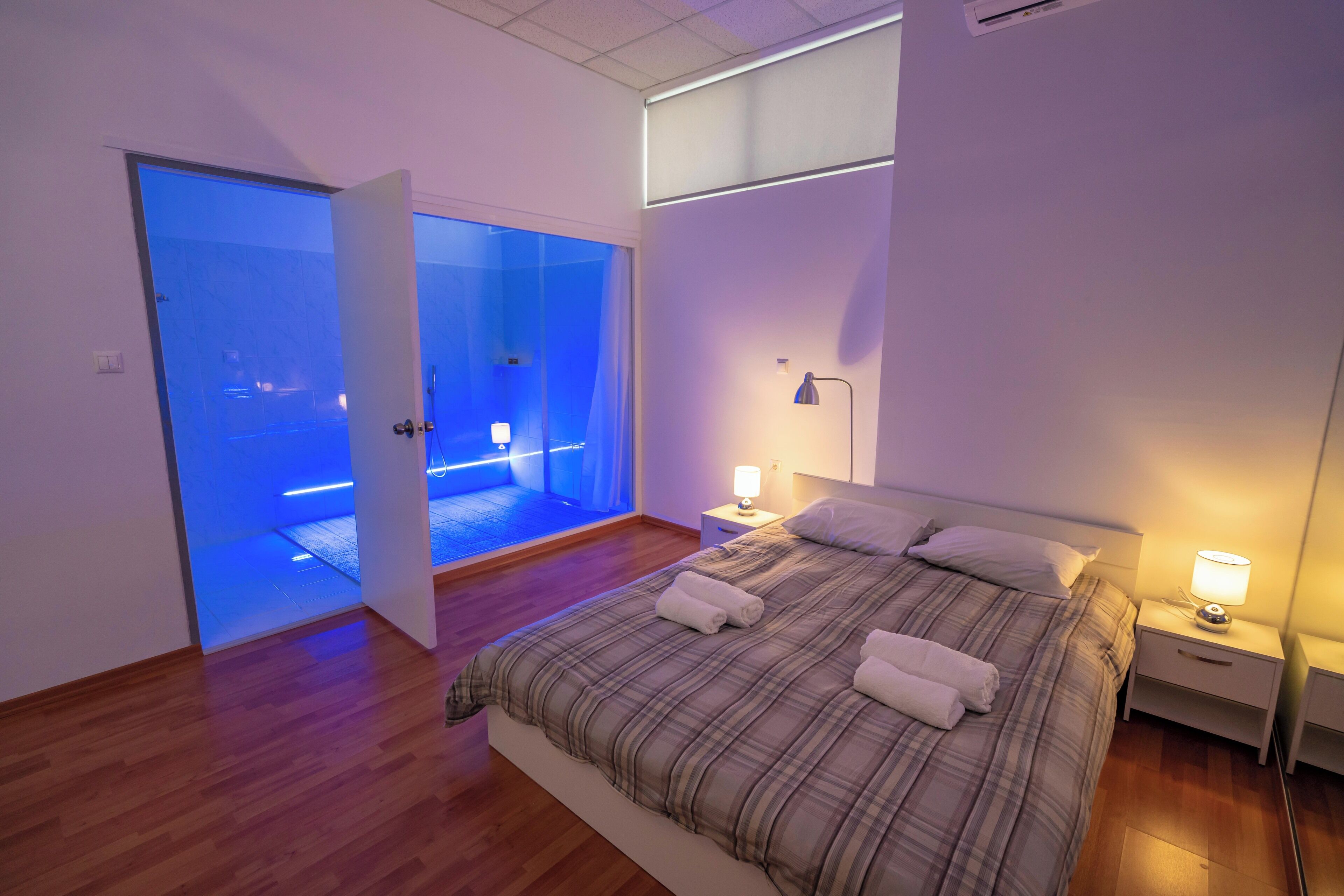 Un dormitorio moderno con una cama grande, mesitas de noche con lámparas y una puerta de cristal que da a un baño.