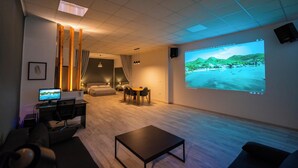 Una habitación de hotel moderna con una pantalla grande, un escritorio con computadora, una zona de estar confortable y un espacio para comer.