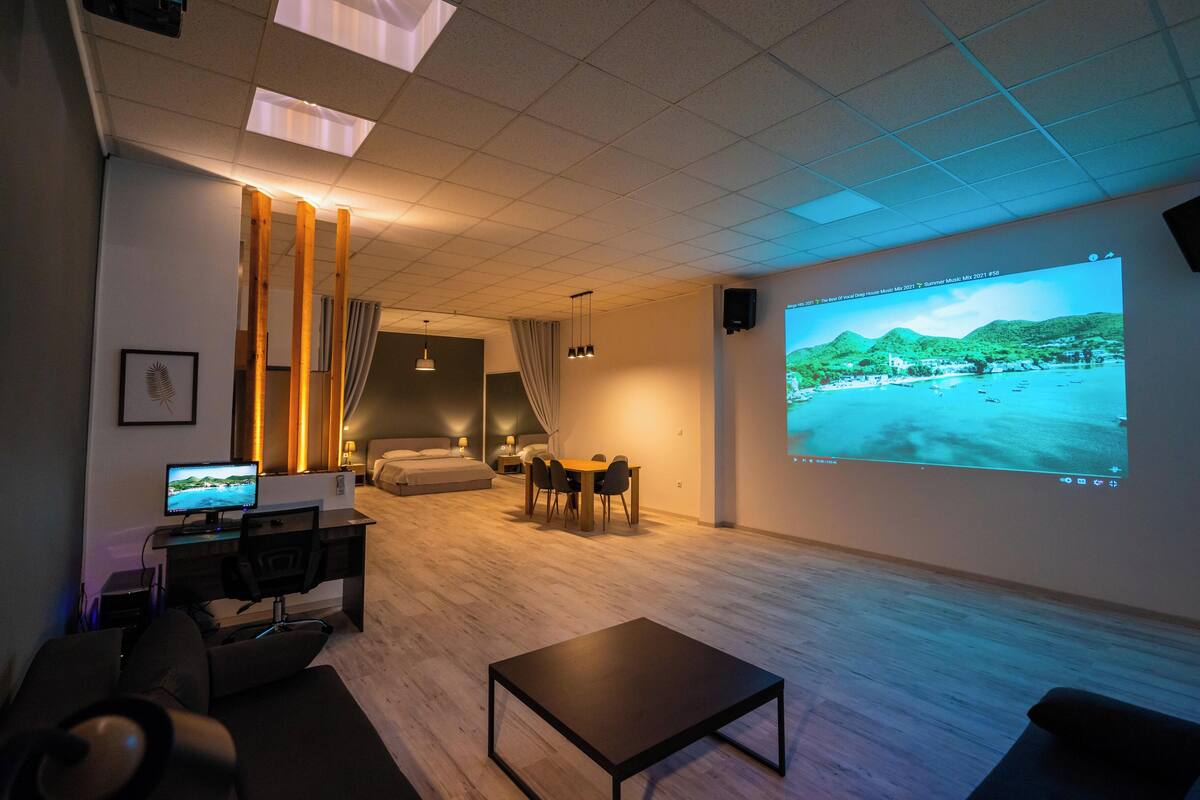 Ett modernt hotellrum med en stor tv-skärm, ett skrivbord med en dator, en bekväm sittgrupp och en plats för måltider.