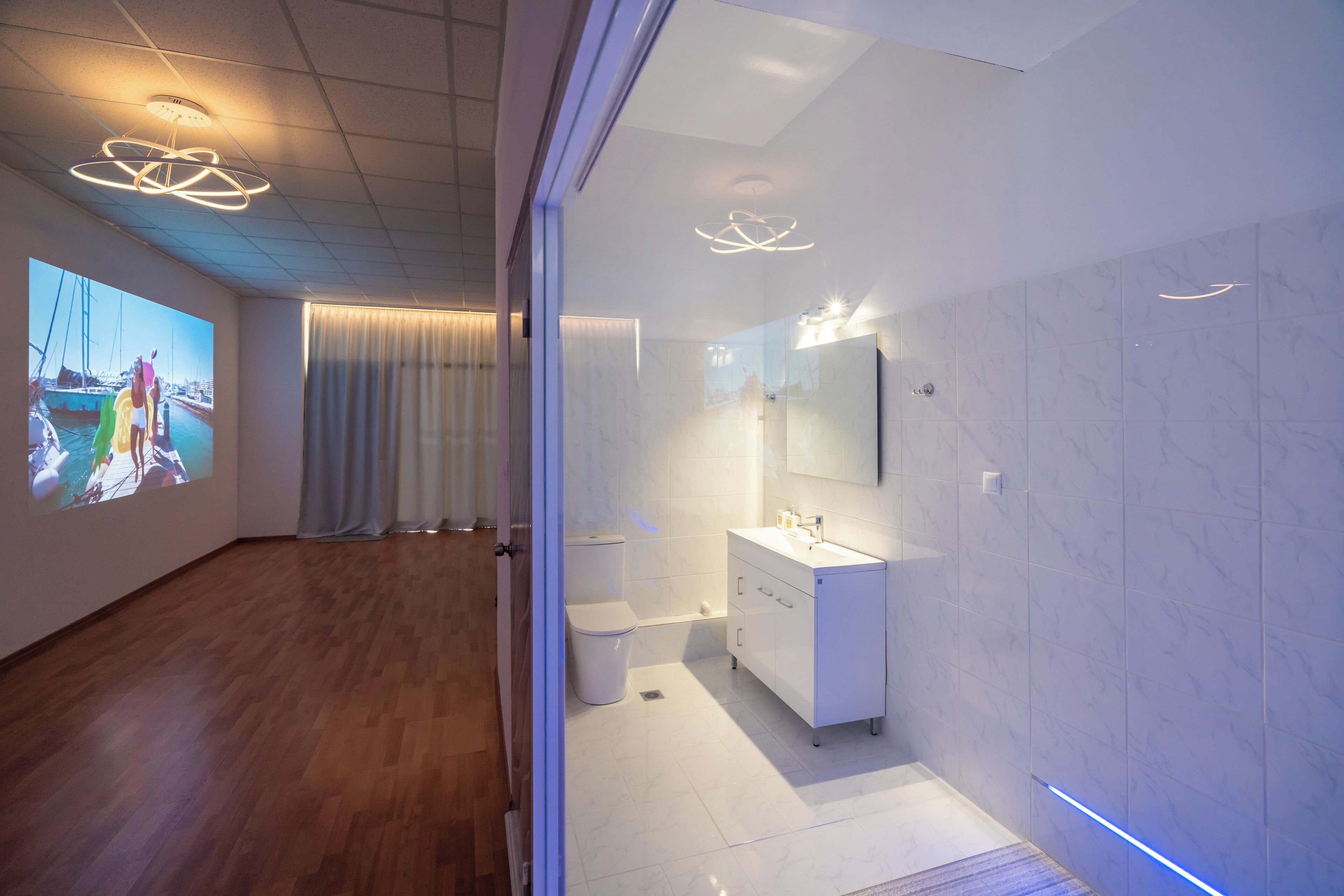 A modern bathroom with a large mirror, white fixtures, and a projection screen on the wall.