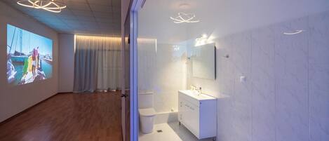 A modern bathroom with a large mirror, white fixtures, and a projection screen on the wall.