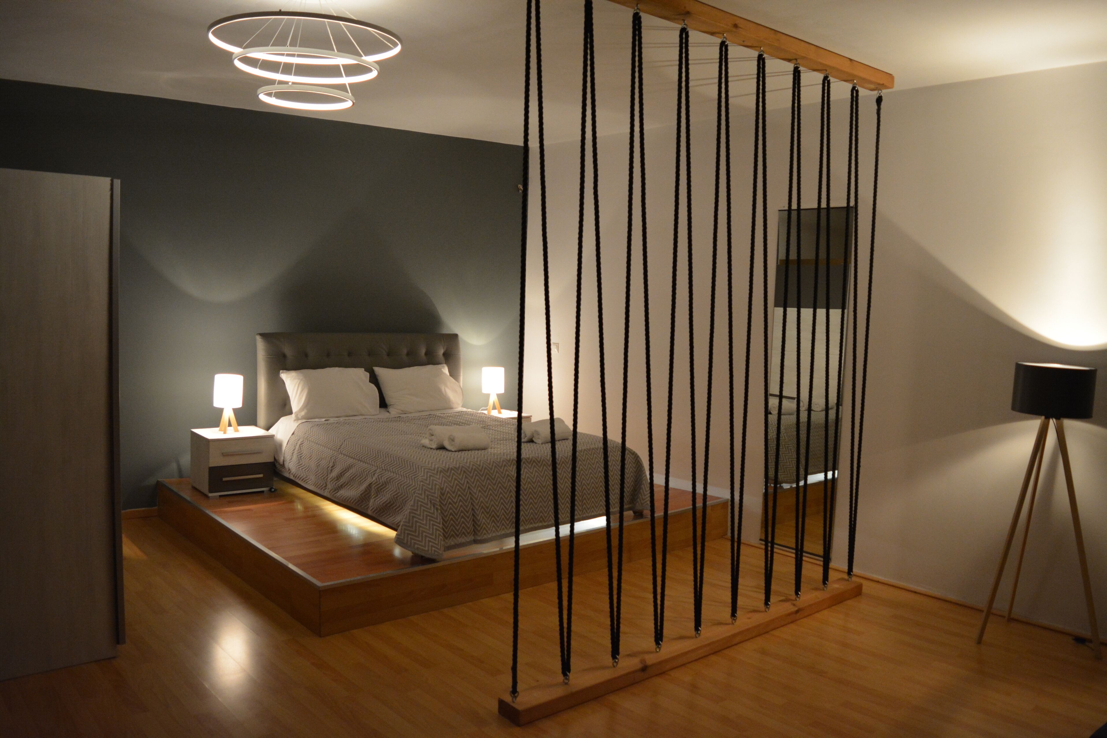 Quarto moderno com cama, mesas de cabeceira e luminária suspensa.