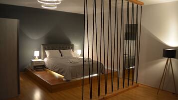 Quarto moderno com cama, mesas de cabeceira e luminária suspensa.