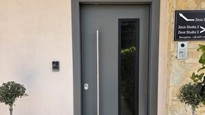 Una entrada moderna con una puerta gris, un letrero de recepción y dos plantas en macetas.