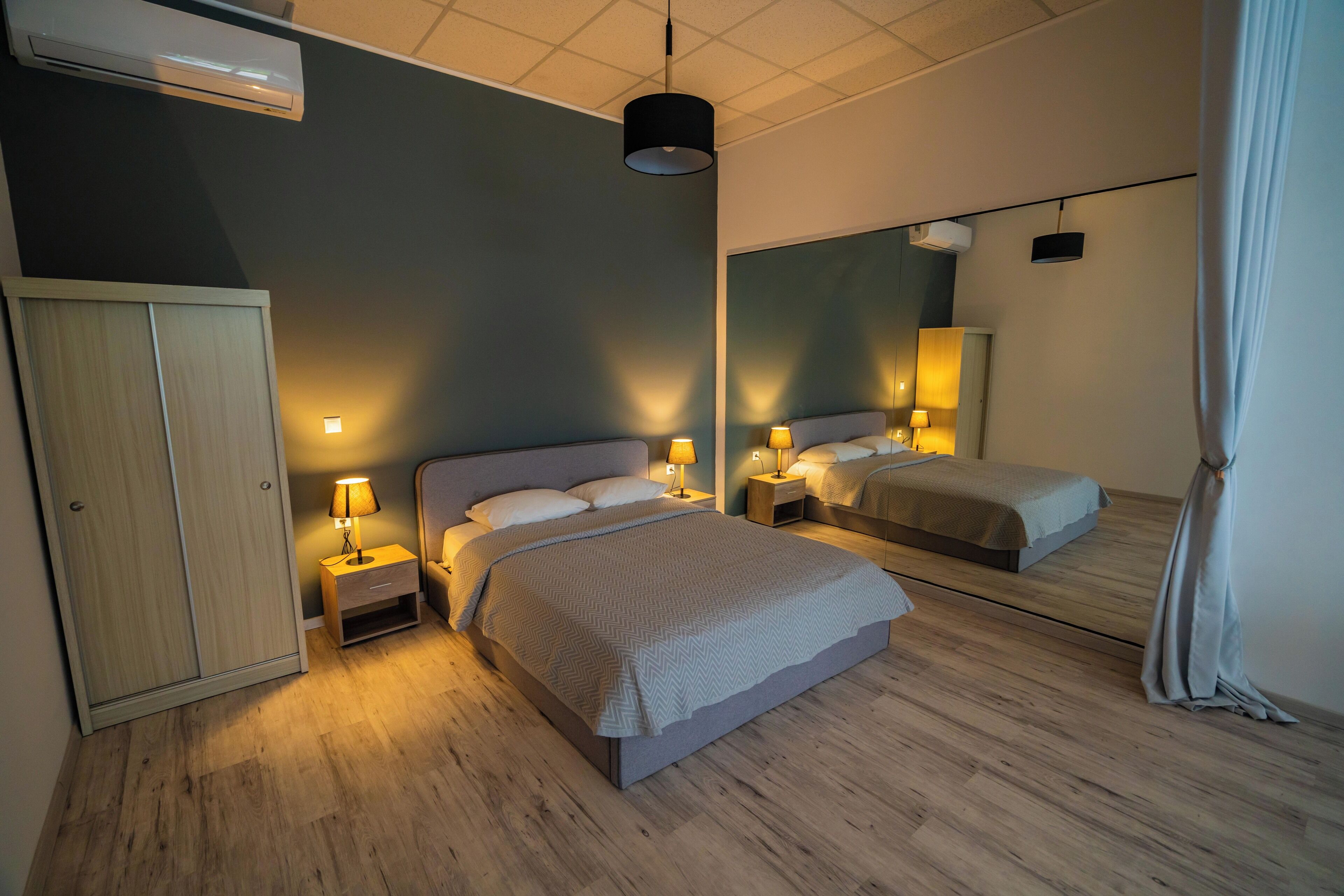 Una habitación de hotel moderna con una cama grande, mesitas de noche con lámparas, un armario y un espejo.