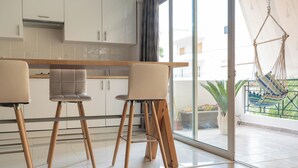 Una cocina moderna con armarios blancos, encimera de madera y puerta de vidrio que da a un balcón con una hamaca.