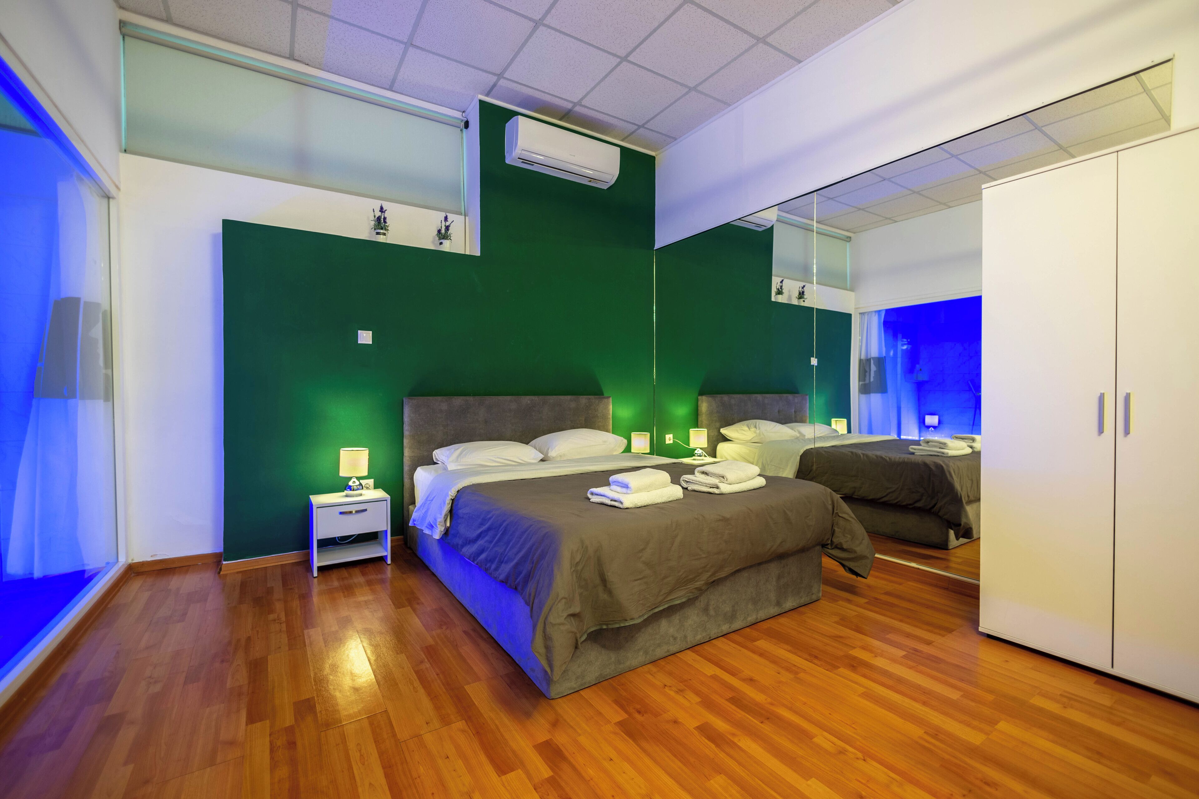 Een moderne slaapkamer met een groot bed, een nachtkastje, een garderobe en een spiegel.