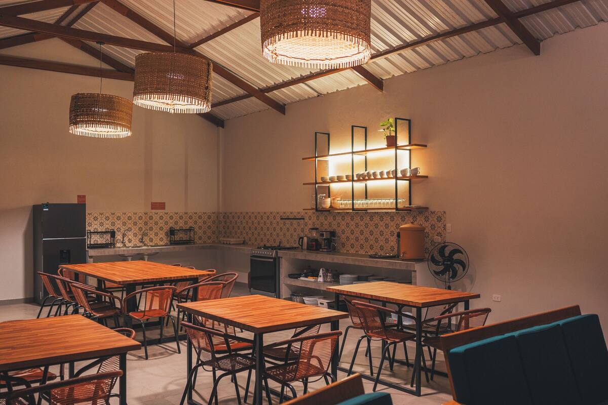 A restaurant with wooden tables and chairs, a kitchen area, and hanging wicker chandeliers.