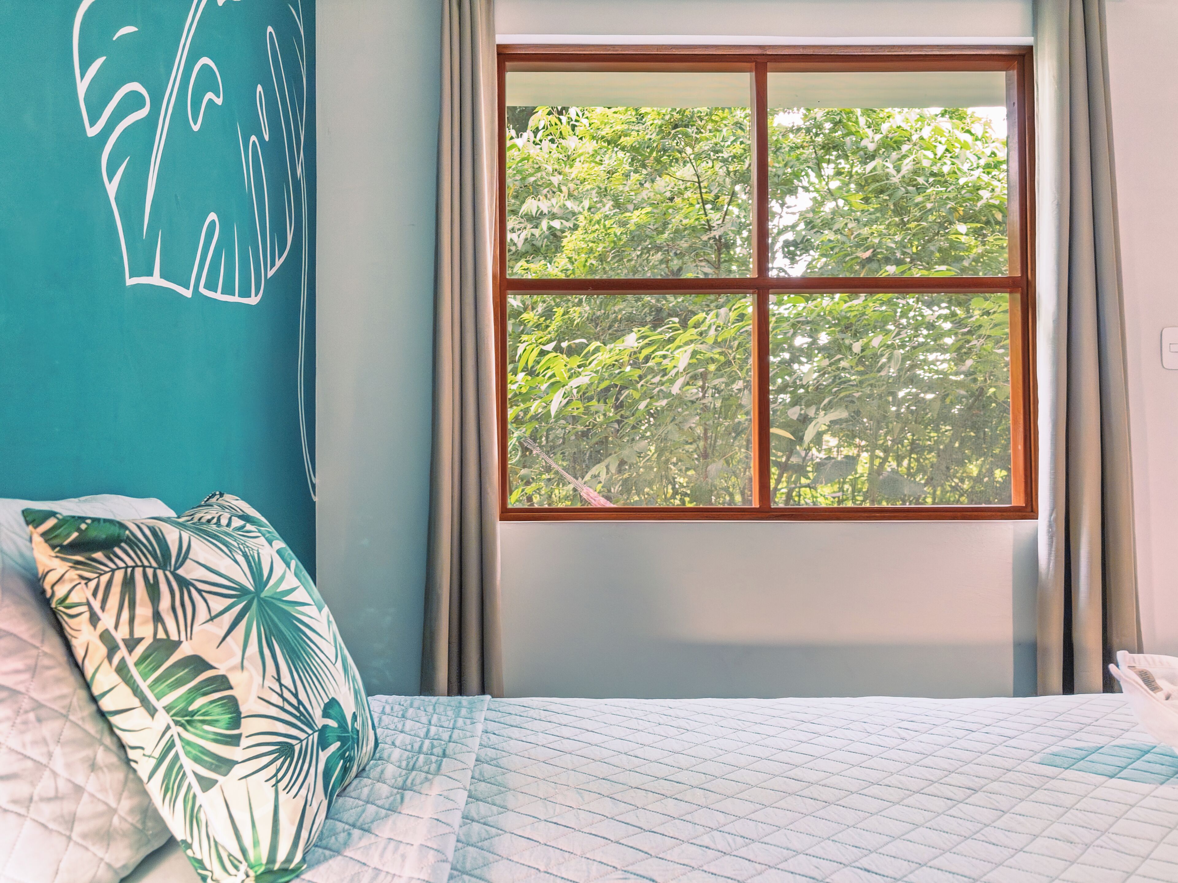 Un dormitorio con cama, ventana con vista a árboles y pared con diseño geométrico.