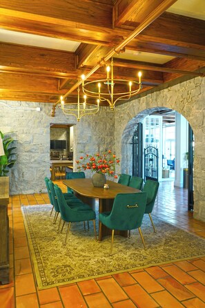 A dining area with a wooden table, green upholstered chairs, a chandelier, and a stone wall. - Santa Rosa Stonehouse Private Wine Country Retreat (Santa Rosa)