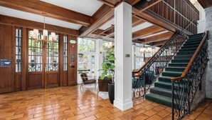 A spacious lobby with a wooden floor, a staircase with black iron railings, and a view of the outdoors through large windows. - Santa Rosa Stonehouse Private Wine Country Retreat (Santa Rosa)