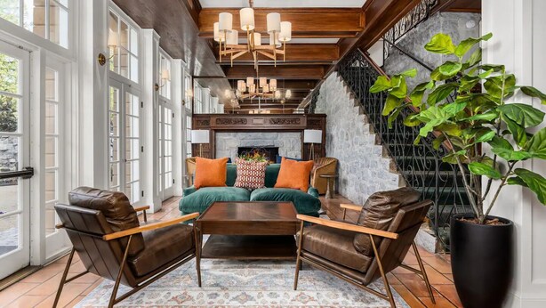 A spacious living room with a large sofa set, a coffee table, and leather armchairs. There is a fireplace with a mantel, a staircase with a wrought iron railing, and a large potted plant. - Santa Rosa Stonehouse Private Wine Country Retreat (Santa Rosa)