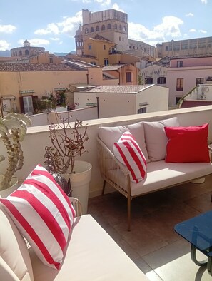 A rooftop terrace with a sofa and cushions, a table, and potted plants. - Gathering on the terrace with private parking (Palermo)