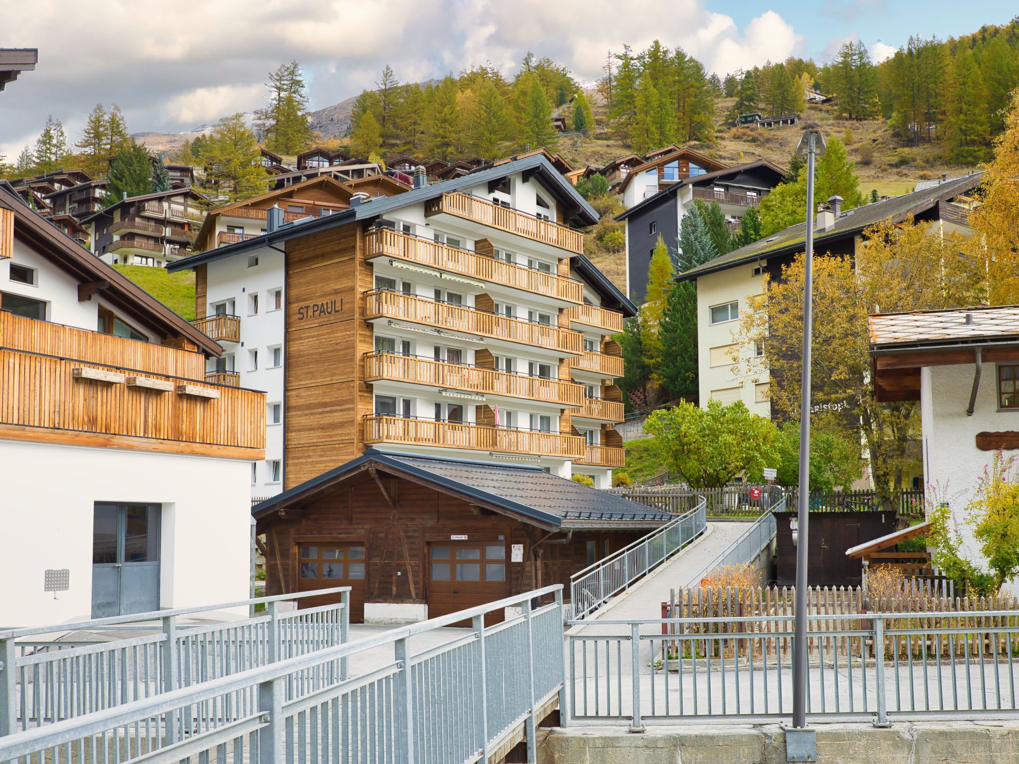 A multi-story hotel with wooden balconies, a ski lift in the background, and a mountainous landscape.