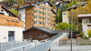 Un hôtel à plusieurs étages doté de balcons en bois, avec un télésiège visible au loin et un paysage montagneux en toile de fond.
