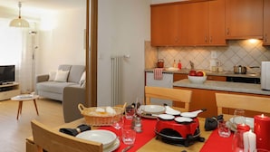 Un coin repas avec une nappe rouge, des chaises en bois et une cuisine en arrière-plan.