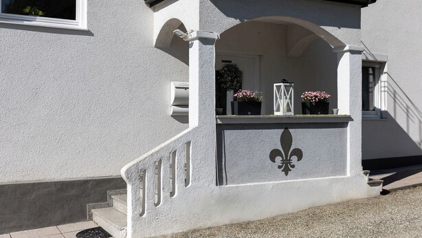A building with a white facade, a balcony with a railing, and a door with a wreath. - Guest at Gastel's FeWo 3-6 persons gladly workers or fitters (Fischach)