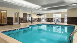 Una piscina interior con agua azul cristalina, rodeada de sillones de descanso y una zona de estar cubierta.