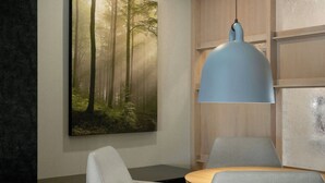 Un interior moderno con un comedor, un cuadro de gran tamaño con temática forestal en la pared y una lámpara colgante azul.