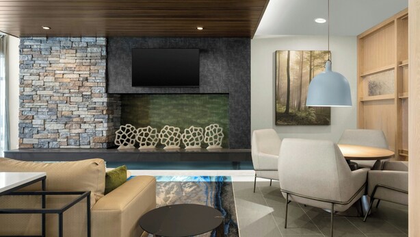 Una sala de estar moderna con una pared de piedra, una chimenea y un televisor de pantalla plana. Hay sofás, una mesa de centro y un comedor con sillas.