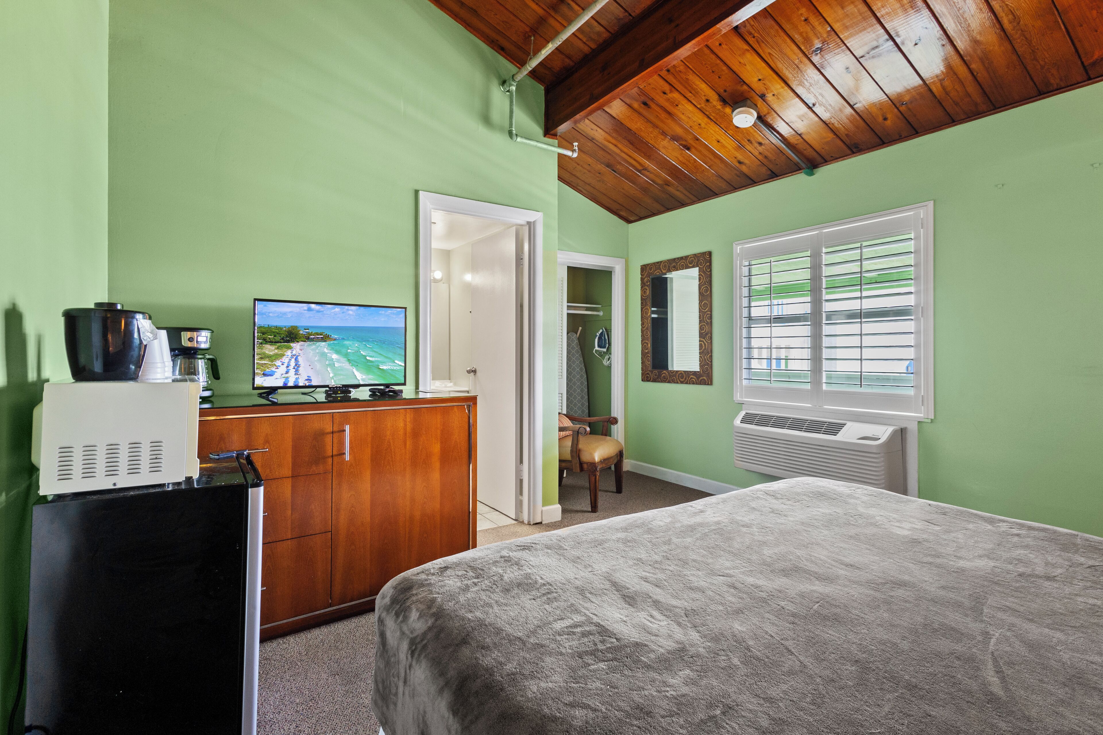 Une chambre à coucher avec un lit, un bureau avec un ordinateur, une chaise et une fenêtre avec des stores.