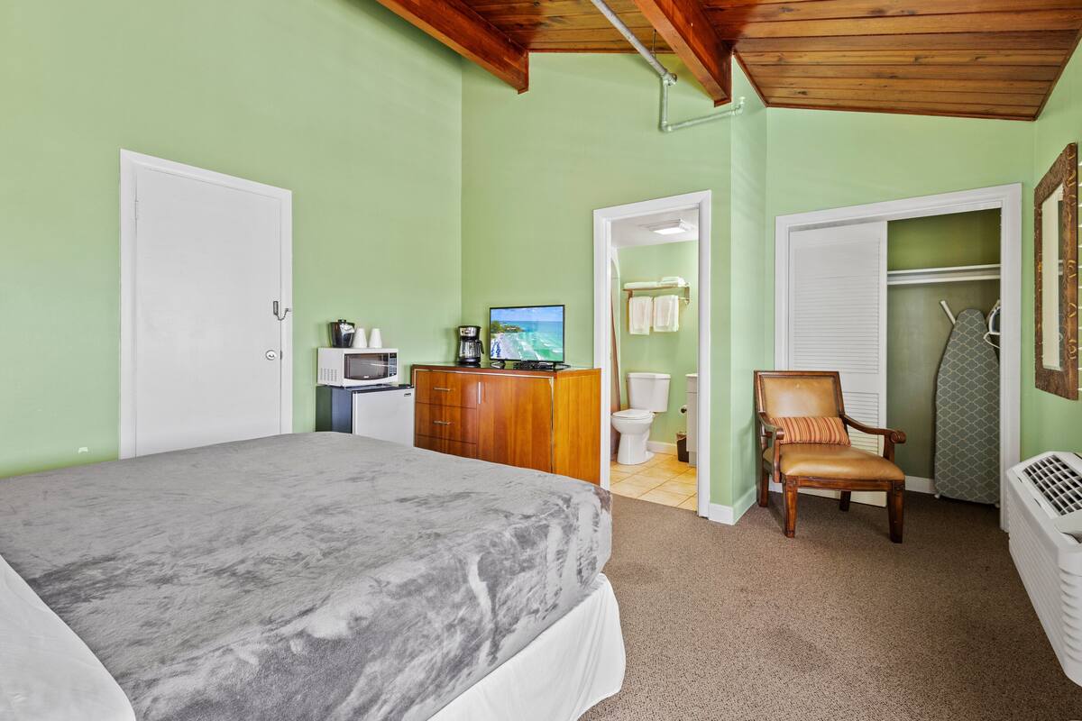 A bedroom with a bed, a wooden dresser, a television, and a chair.