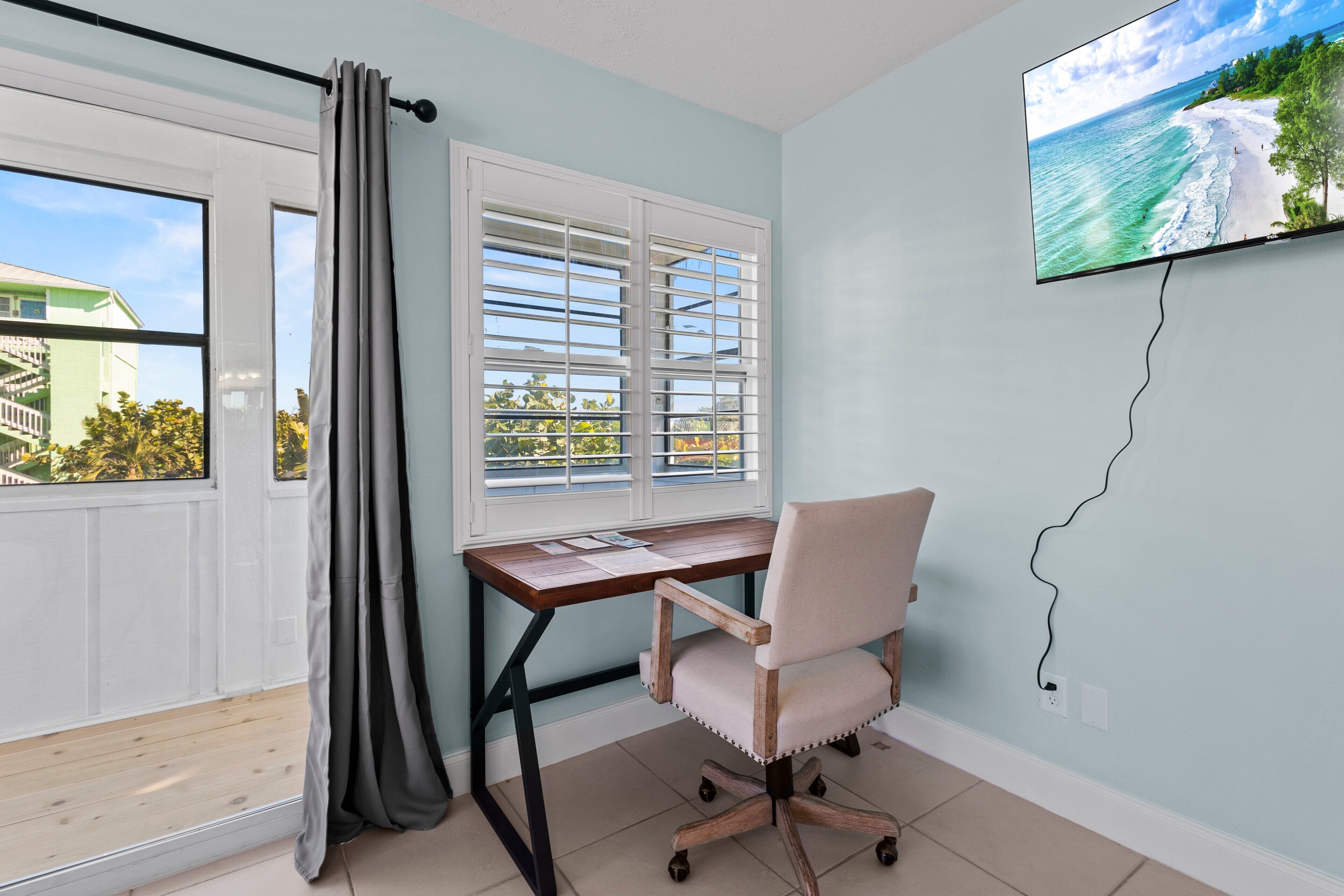 A room with a desk, chair, and a TV displaying a beach scene.
