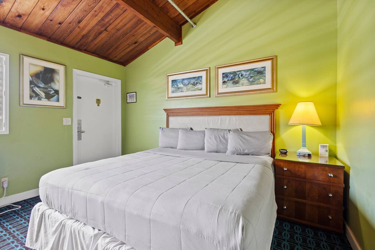 A hotel room with a large bed, a wooden headboard, a nightstand with a lamp, and two framed pictures on the wall.
