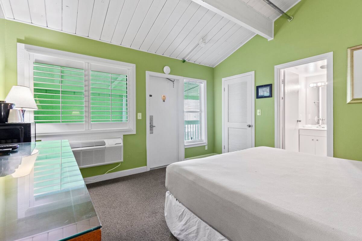 A bedroom with a bed, a desk with a lamp, and a window with blinds.
