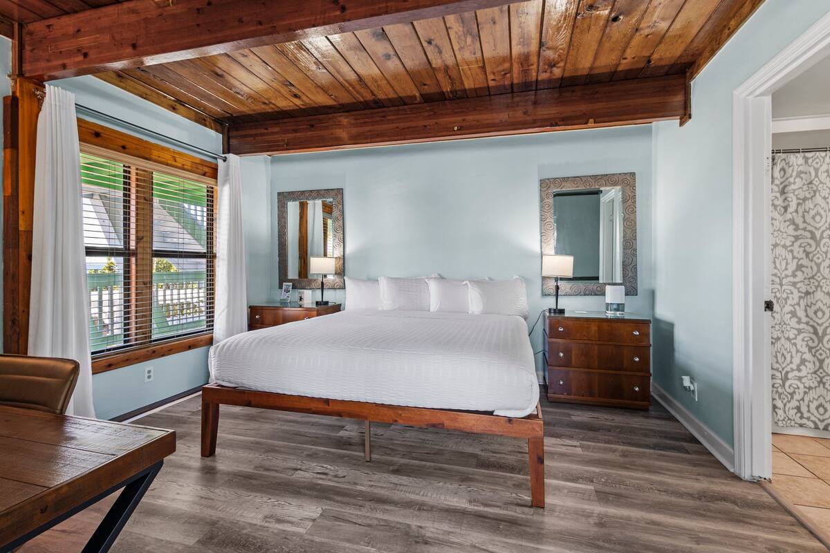 A bedroom with a wooden bed, a nightstand, a dresser, and a window with blinds.
