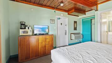 A bedroom with a wooden dresser, a bed, a television, and a door with a blue shutter.