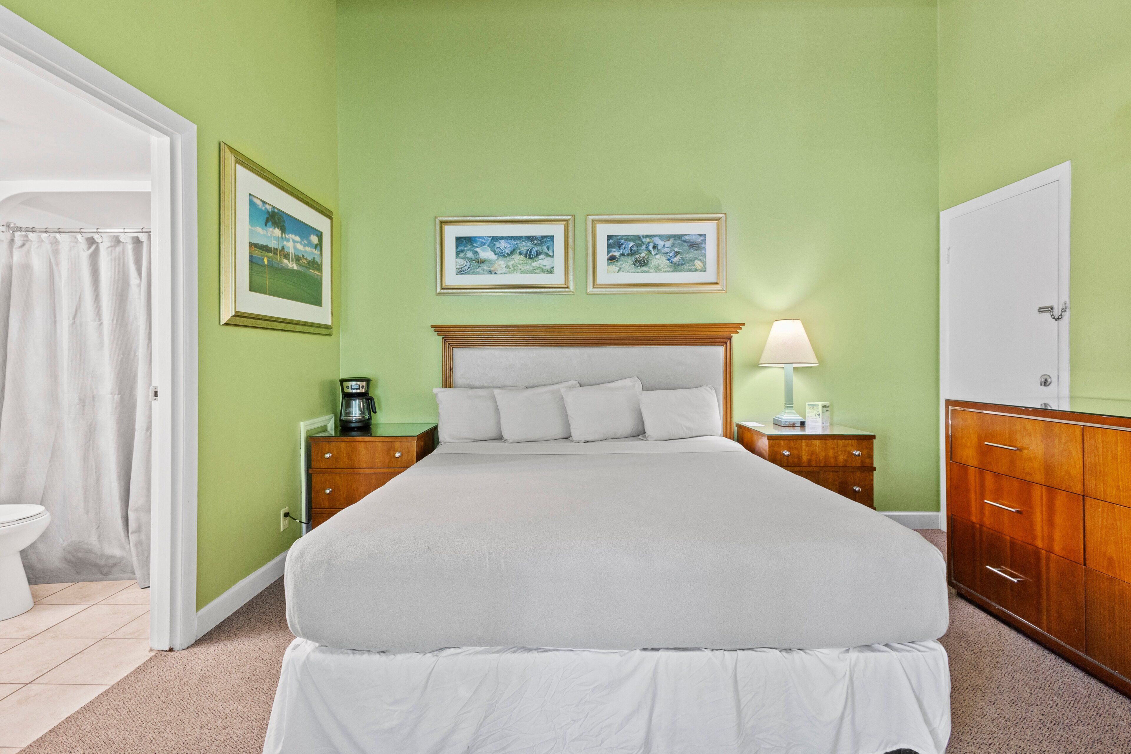 Une chambre à coucher bien rangée, avec un lit, des tables de chevet, une commode et deux tableaux encadrés accrochés au mur.