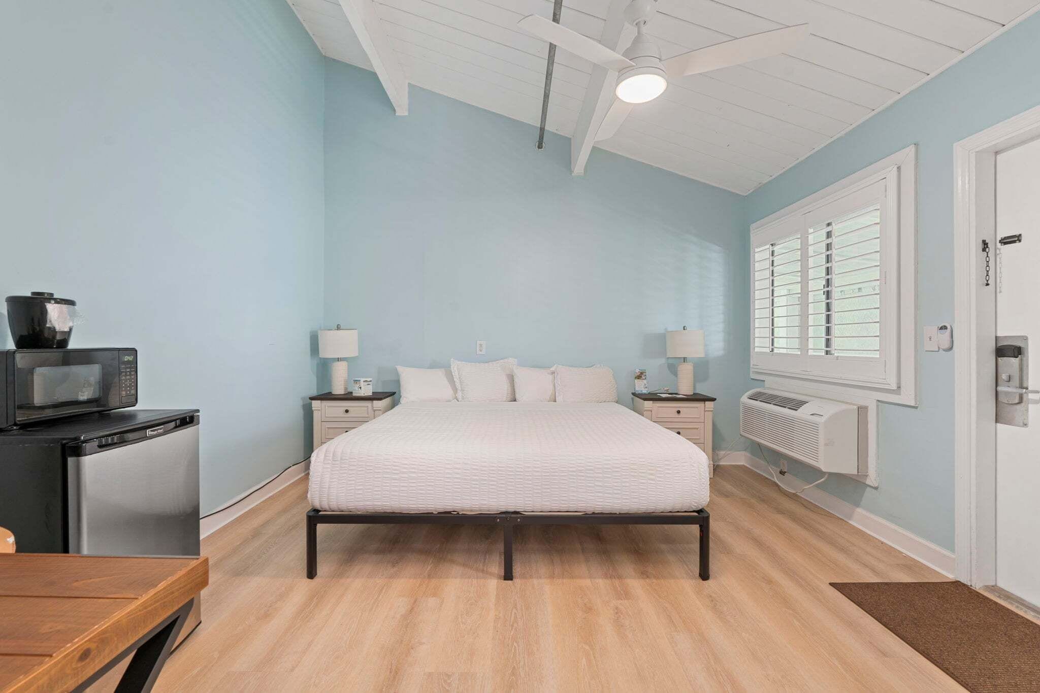 Un dormitorio con cama, mesitas de noche, televisor y ventana con persianas.
