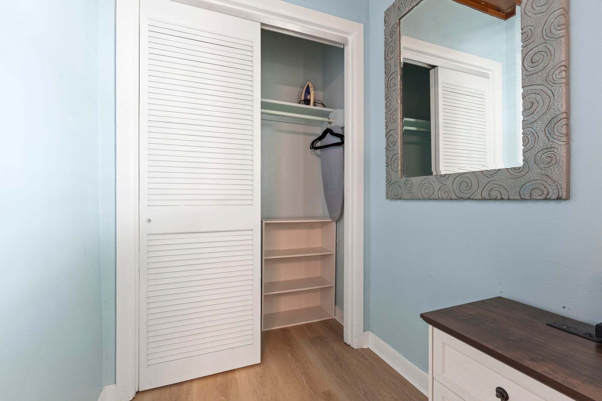 A walk-in closet with a mirrored wardrobe, a hanging rack, and a wooden floor.