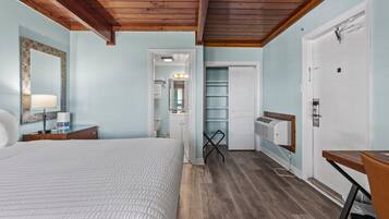 Een slaapkamer met een bed, nachtkastje en spiegel. Er is een deur naar een badkamer en een kledingkast.