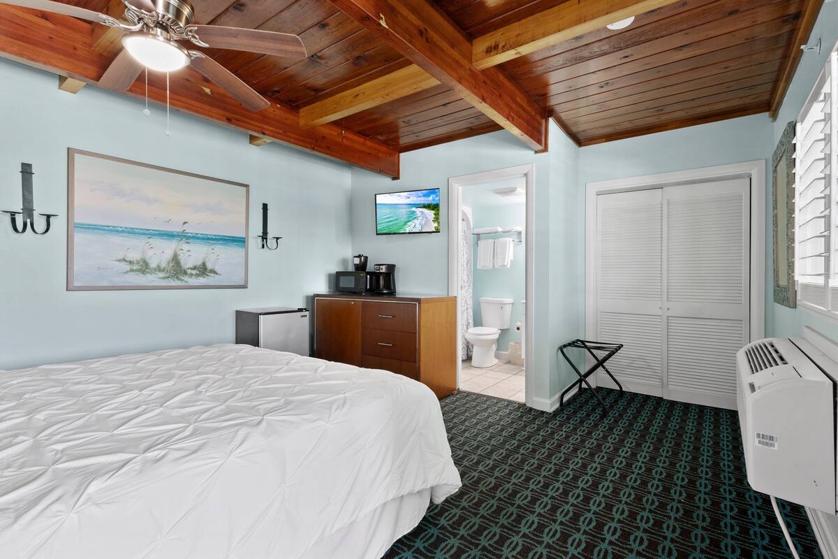 A bedroom with a bed, a wooden wardrobe, a television, a toilet, and a white air conditioning unit.