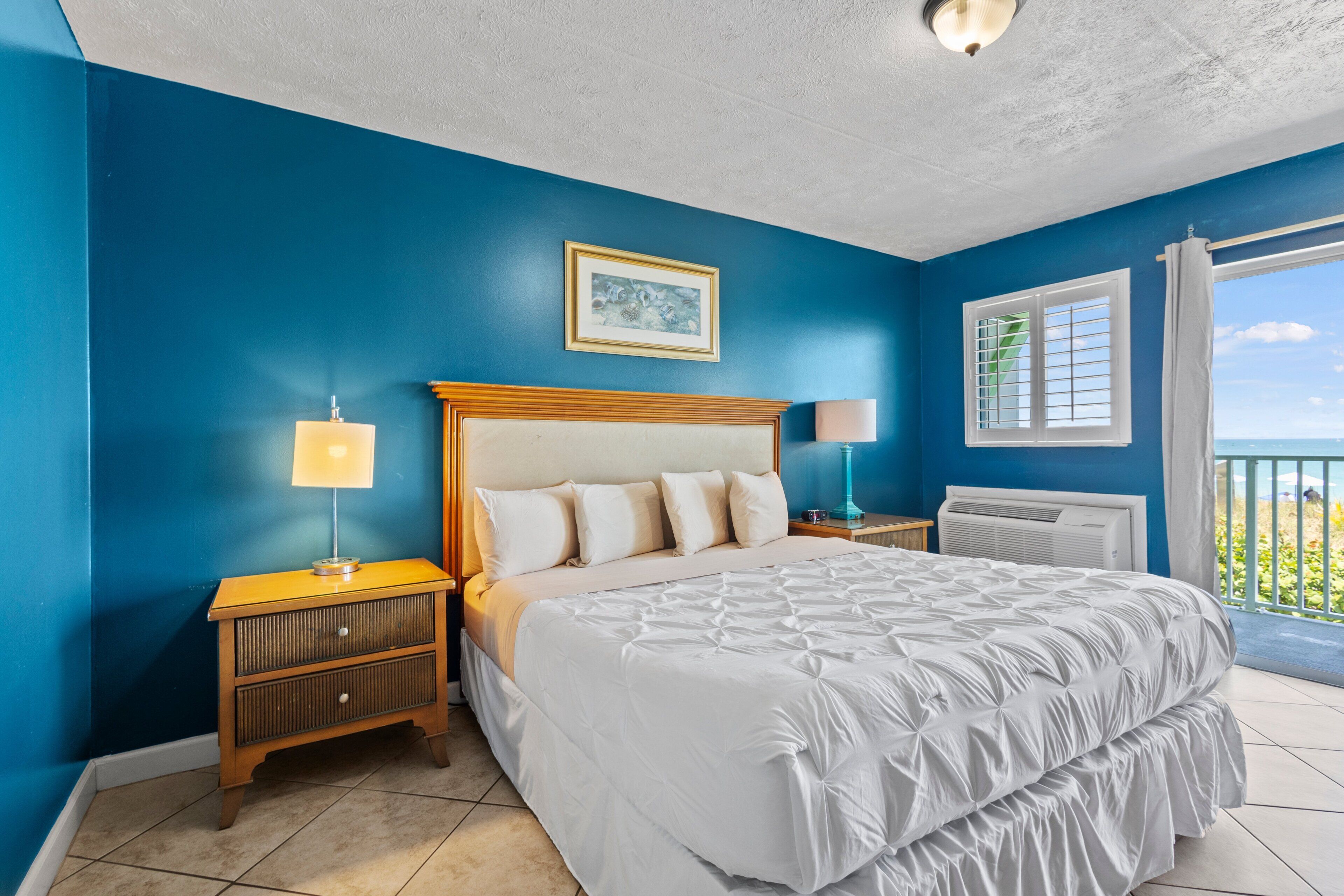 A bedroom with a large bed, two bedside tables, a window with a view, and a ceiling light.