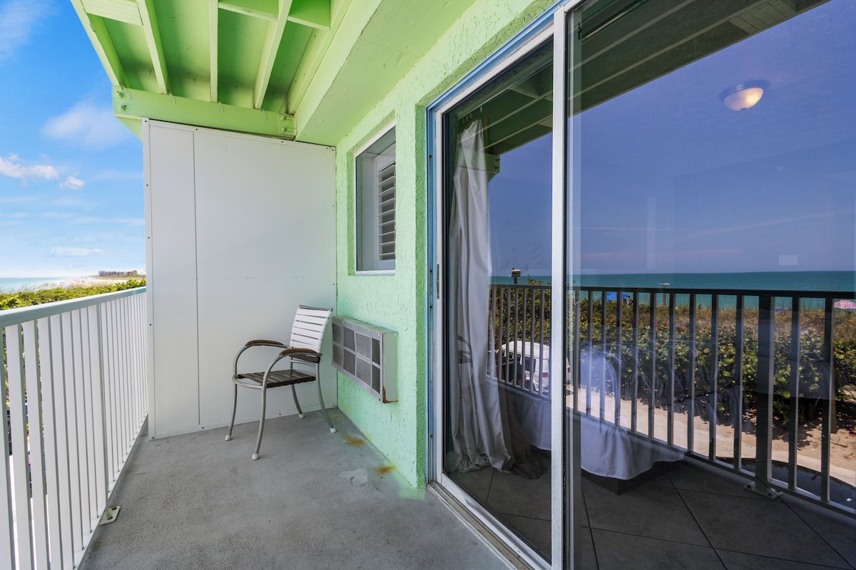 A balcony with a view of the ocean, a chair, and a table with a tablecloth.