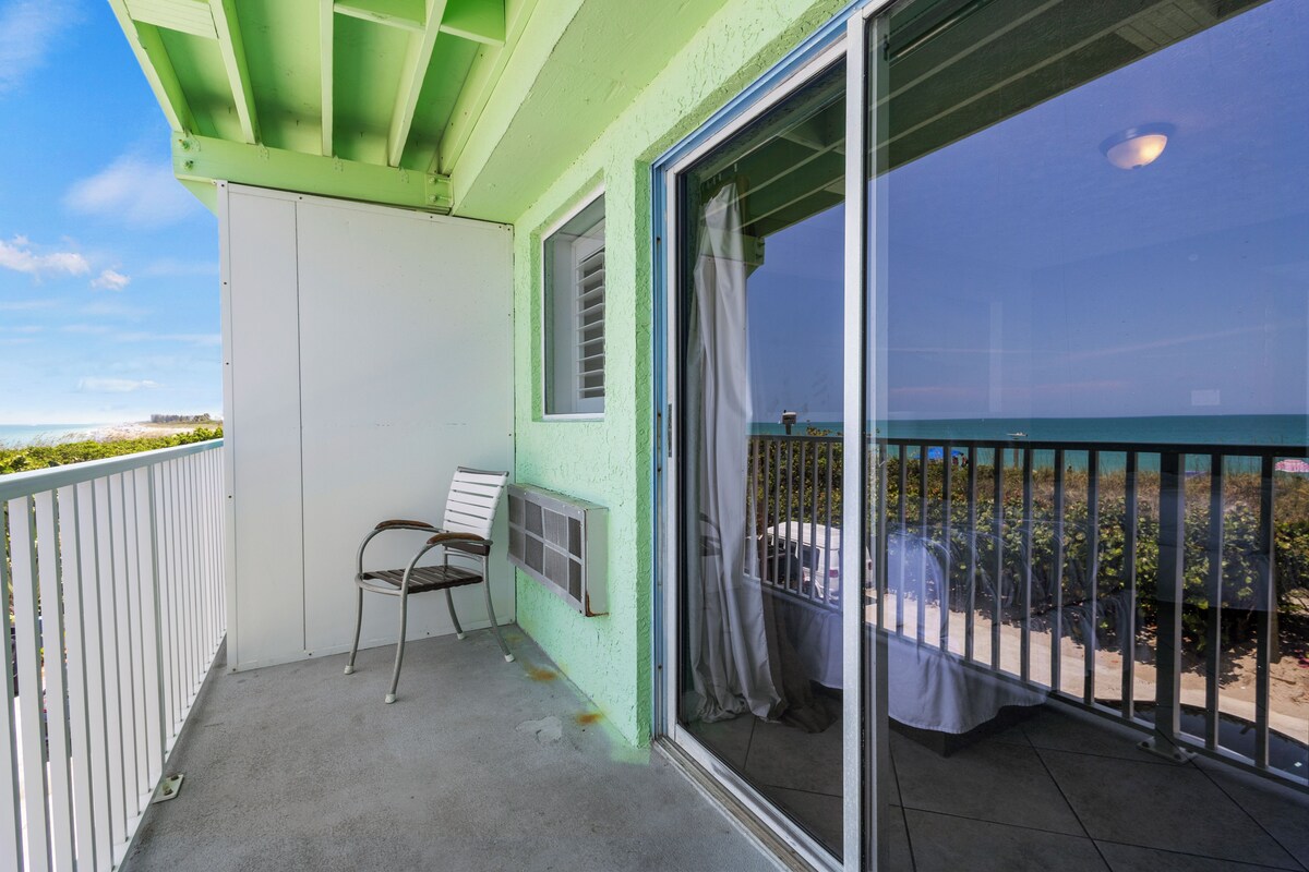 A balcony with a view of the ocean, a chair, and a table with a tablecloth.